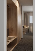 Una habitación de hotel moderna con un armario de madera, un escritorio con lámpara, una silla y una ventana con cortinas.
