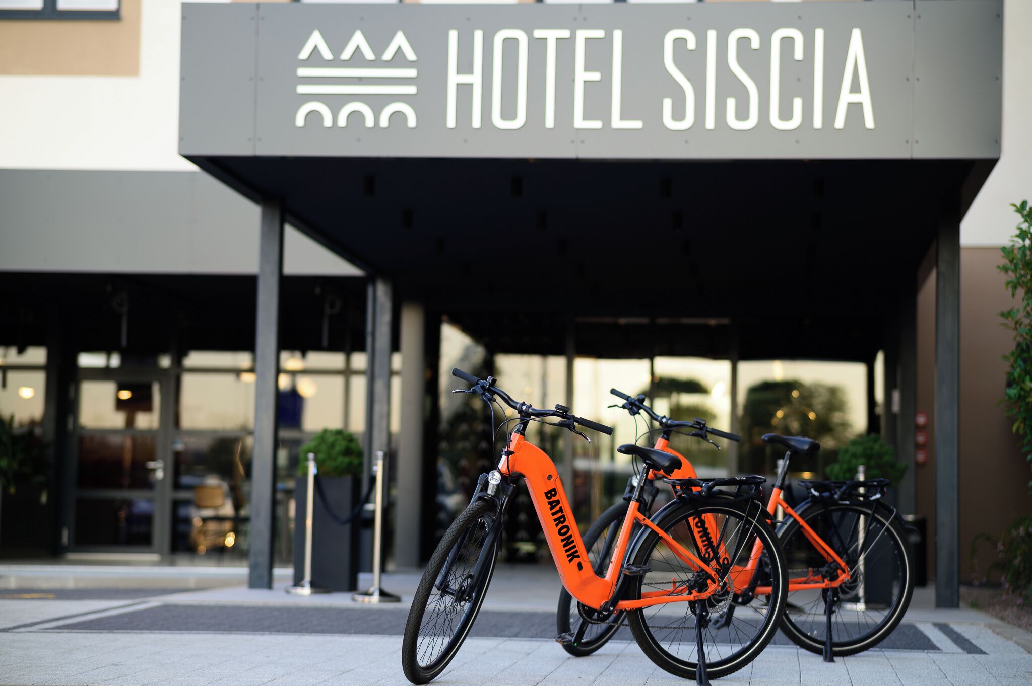 Een hotelentree met een bord waarop 'HOTEL SISCIA' staat en drie fietsen ervoor geparkeerd.