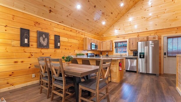 A wooden cabin interior with a dining area, kitchen, and a refrigerator.