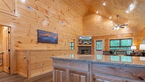 A wooden interior with a kitchen island, wooden cabinets, a fireplace, and a ceiling fan.