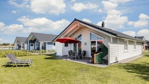A single-story house with a patio, a red umbrella, and a lawn with two lounge chairs. - Ferienhaus in Dagebuell im skandinavischen Stil (Dagebüll)