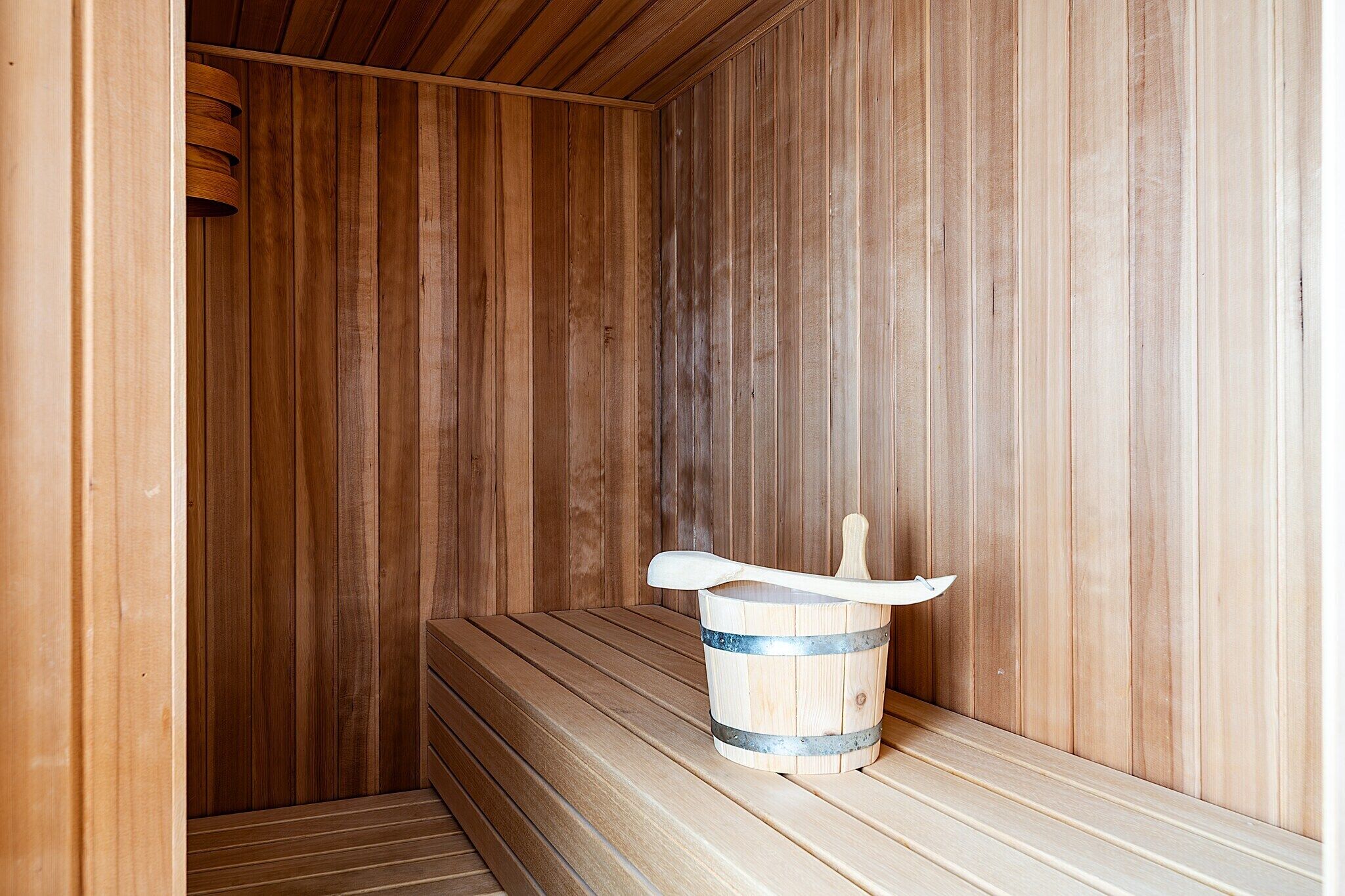 Eine Holzsauna mit Bänken und einem Holzfass mit Schöpfkelle.