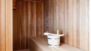 Eine Holzsauna mit Bänken und einem Holzfass mit Schöpfkelle.