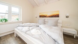 A bedroom with a large bed, a window, a bedside table, and a wall-mounted lamp. - Ferienhaus in Dagebuell im skandinavischen Stil (Dagebüll)