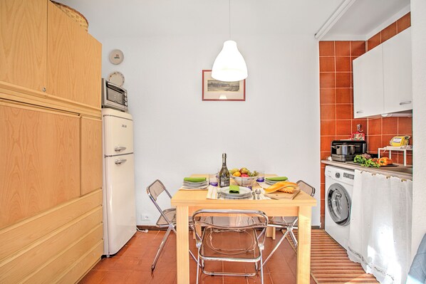 A compact kitchen with a wooden cabinet, a white refrigerator, a hanging pendant light, and a dining table with chairs. - Appartamento Chez Mavi Cond Il (Sauze d'Oulx)