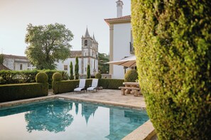 A swimming pool with lounge chairs and a bench, surrounded by neatly trimmed hedges and a building with a bell tower in the background. - Quinta do Bonfim - a historic refuge in the heart of Portalegre. (Portalegre)
