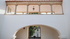Uma área externa coberta com telhado de azulejos, colunas e um portão.