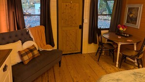 A cozy room with a dark-colored sofa, a wooden door, a dining table with chairs, and a painting on the wall. - Black Mtn Stomping Ground's Falcon's Perch with Long-Range Views (Black Mountain)