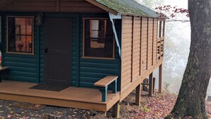 A wooden cabin with a porch, two windows, and a door. - Black Mtn Stomping Ground's Falcon's Perch with Long-Range Views (Black Mountain)