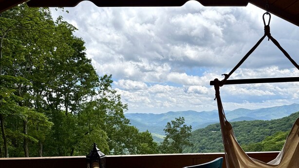 A wooden deck with a table and chairs, a hanging hammock, and a lantern. - Black Mtn Stomping Ground's Falcon's Perch with Long-Range Views (Black Mountain)