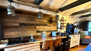 A rustic kitchen with wooden walls, a bar area with stools, a coffee station, and a view of the outdoors. - Black Mtn Stomping Ground's Falcon's Perch with Long-Range Views (Black Mountain)