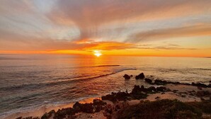 Ein Sonnenuntergang über einer felsigen Küstenlinie, während Wellen an den Strand schlagen.