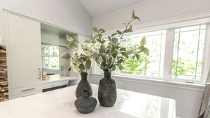 A kitchen with white cabinets, a marble countertop, and three vases with flowers. - Luxury 4BR Stay with Swim Spa, Golf & Fireplaces (Caledon)