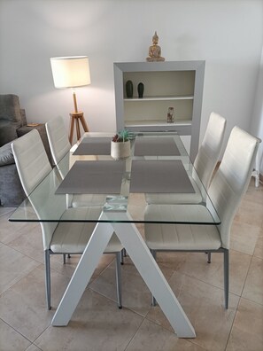 A modern dining area with a glass table, white chairs, and a decorative Buddha statue. - Apartment 'Solnerja' with Mountain View, Private Terrace and Wi-Fi (Nerja)