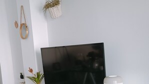 Uma televisão de tela plana sobre um armário branco com gavetas, uma pequena planta em vaso e um abajur.