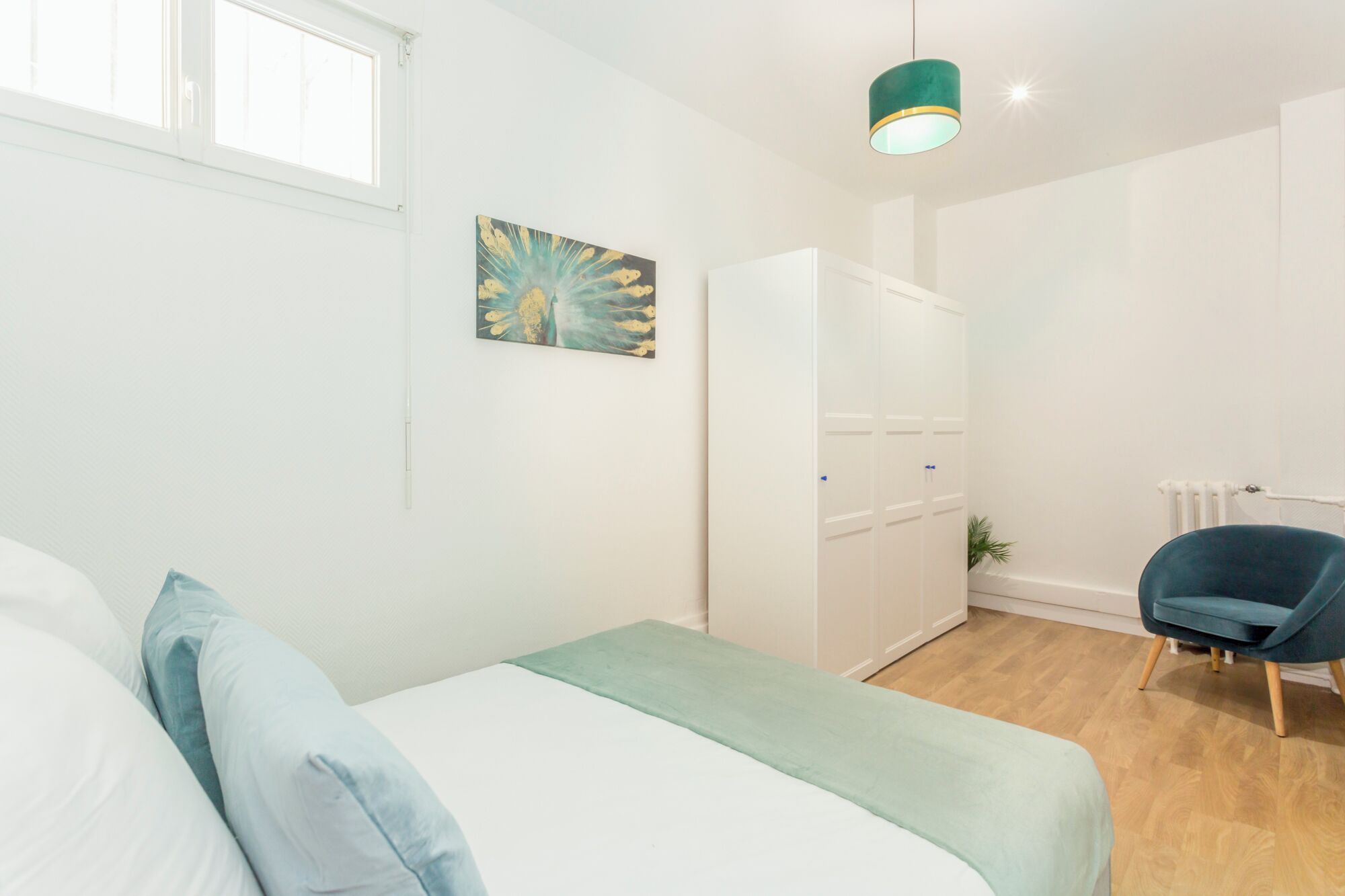 Un dormitorio con cama, una silla, un armario y un cuadro en la pared.