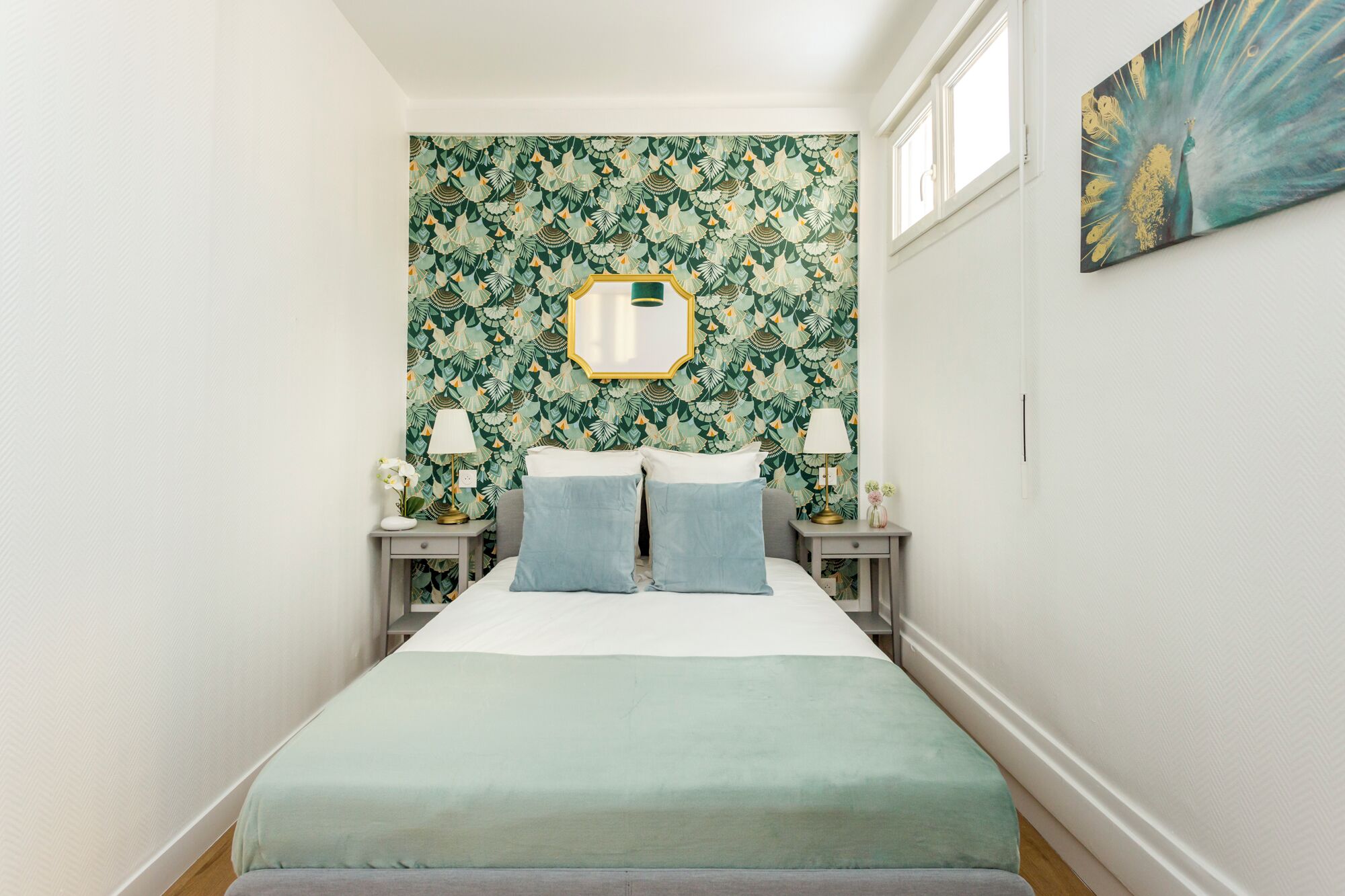 A bedroom with a bed, two bedside tables with lamps, a mirror, and a floral wallpaper.