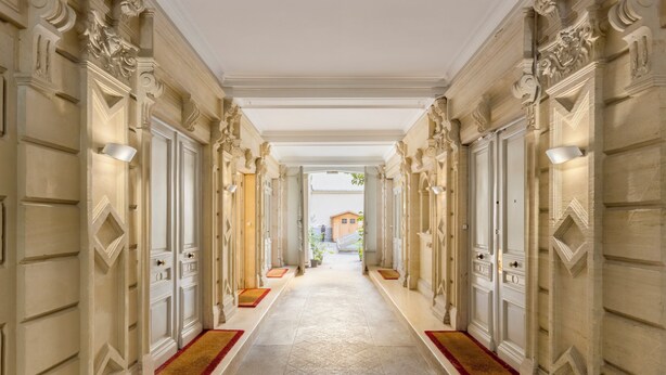 Un'ampia sala con colonne decorate e porte, che conduce a un cortile con una struttura in legno.
