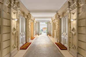 Un amplio pasillo con columnas y puertas decoradas, que da a un patio con una estructura de madera.