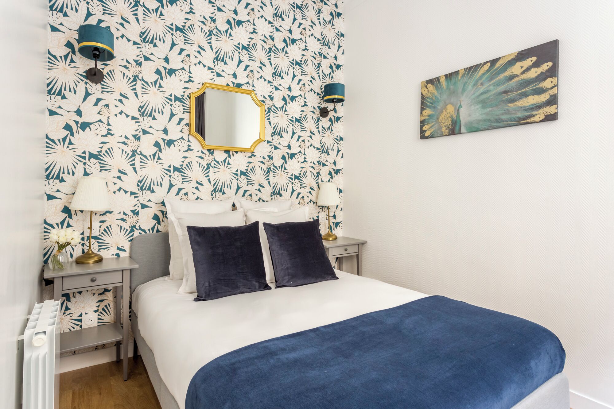 Een slaapkamer met een bed, twee nachtkastjes, een spiegel en een wand met bloemenbehang.
