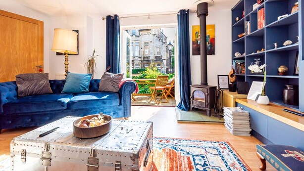 Un salon avec un canapé bleu, une valise ancienne, une bibliothèque et un poêle à bois.