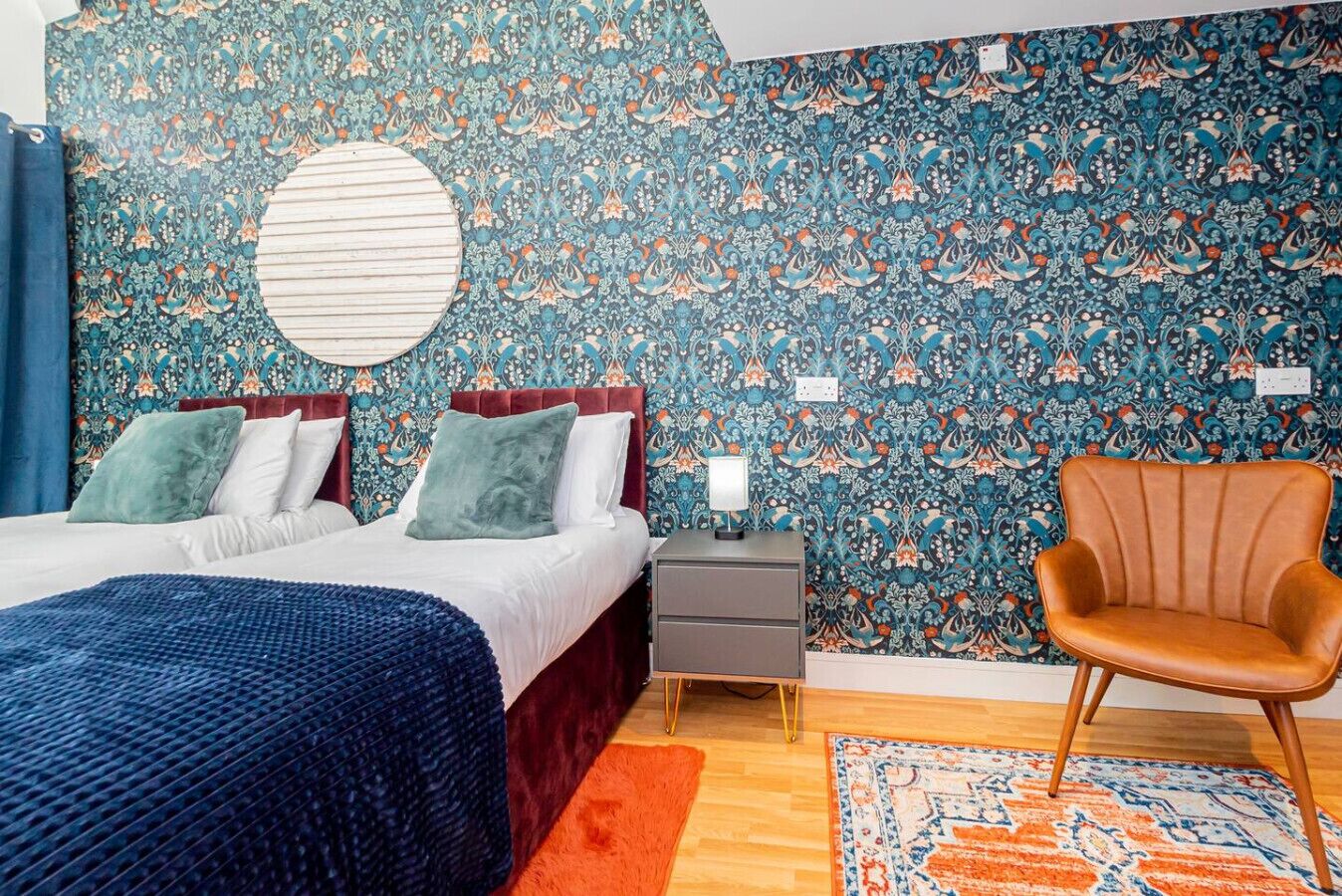 A bedroom with a bed, two bedside tables, a chair, and a patterned wall.