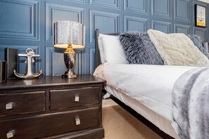 Een slaapkamer met een bed, een nachtkastje, een lamp en een decoratieve anker.