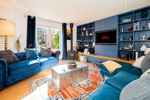 Een moderne woonkamer met een blauwe bank, een televisie en een boekenkast.