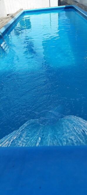 Visão nítida de uma piscina interior com um deck de madeira e paredes revestidas de azulejo.