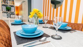 A dining table set with blue bowls, plates, and wine glasses, with a vase of yellow flowers in the center.