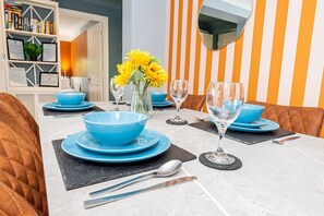 Een eettafel gedekt met blauwe kommen, borden en wijnglazen, met een vaas gele bloemen in het midden.