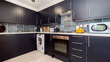 A modern kitchen with dark cabinets, a washing machine, an oven, and a microwave.