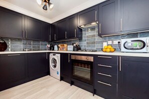 Een moderne keuken met donkere kastjes, een wasmachine, een oven en een magnetron.
