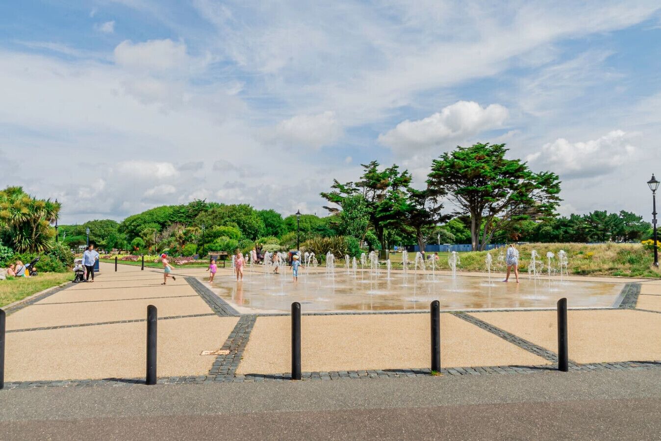 A public park with a water fountain area, paved walkways, and greenery.