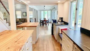 Une cuisine moderne avec des plans de travail en bois, un coin repas avec une table et des chaises, et une vue dégagée grâce à de grandes fenêtres.