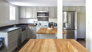 Une cuisine moderne avec des meubles gris, des appareils en acier inoxydable et un plan de travail en bois.