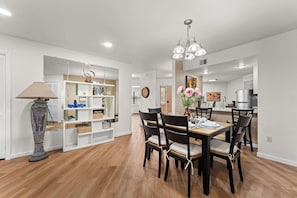 A dining area with a wooden table, chairs, and a chandelier. There is a white shelving unit with decorative items and a lamp. - Fairway Retreat for 6 – Walk-in and Pet Friendly (Branson)