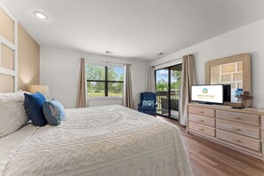 Quarto com cama, televisão, cómoda e vista para o exterior.