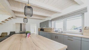 A modern kitchen with a large island, grey cabinets, and a window providing a view. - Ferienhaus in Dagebuell im skandinavischen Stil (Dagebüll)