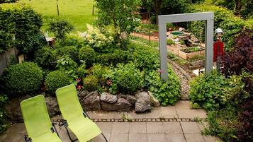 Ein Garten mit einer Metallskulptur, zwei grünen Liegestühlen und einem gepflasterten Weg.
