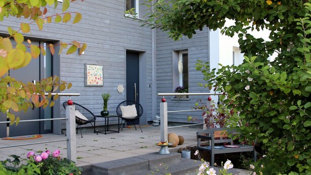 Un bâtiment bleu doté d’un porche, de sièges en plein air et d’un escalier menant à l’entrée.