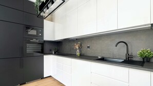 Una cocina moderna con electrodomésticos negros, armarios blancos, encimera negra y salpicadero gris.