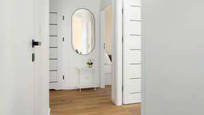 Un pasillo con puertas blancas, un espejo redondo y una pequeña mesa blanca con una planta.
