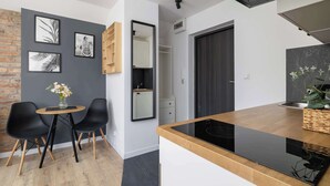 Eine moderne Küche mit schwarzem Arbeitsplatz, Holzschränken und einem eingebauten Ofen. Es gibt einen Essbereich mit einem kleinen runden Tisch und zwei schwarzen Stühlen. Die Küche hat eine Backsteinwand und eine graue Akzentwand mit gerahmten Kunstwerken.