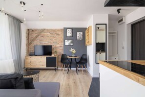 Ein modernes Wohnzimmer mit Fernseher, Esstisch mit Stühlen, Sofa und einem kleinen Beistelltisch.