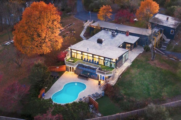Aerial view of the striking modern home surrounded by trees, showing the pool & spacious grounds.