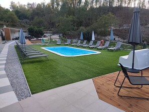 En trädgård med en pool, konstgräs, solstolar och ett trädäck.