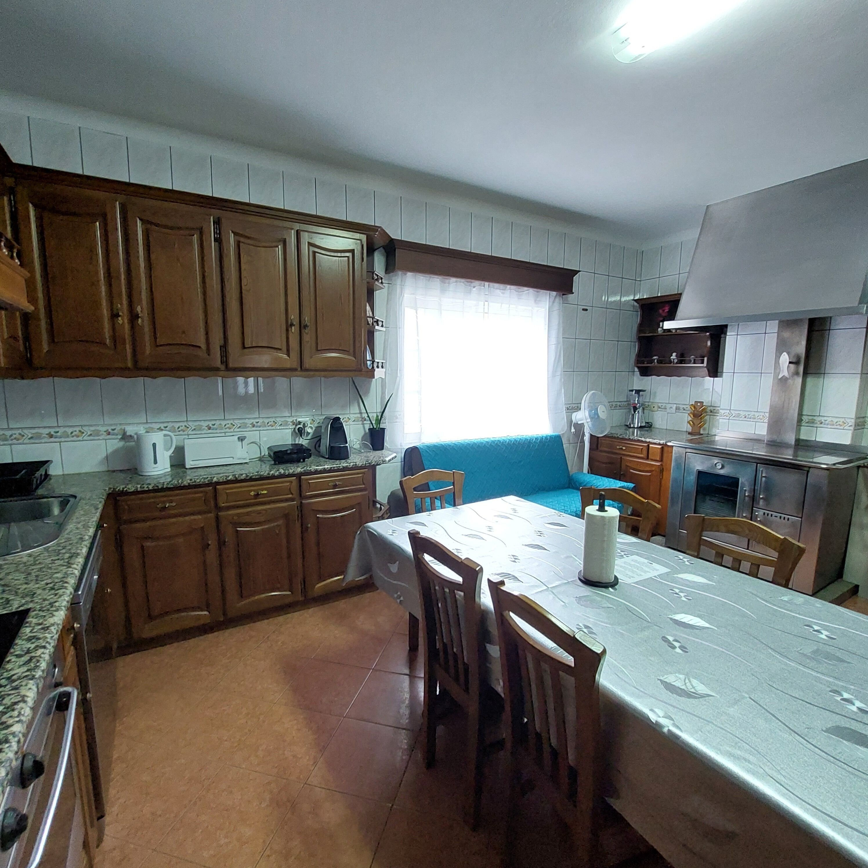 A kitchen with wooden cabinets, a dining table with chairs, a window with curtains, and a tiled backsplash.