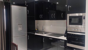 Une cuisine moderne avec des meubles noirs, des appareils en acier inoxydable et un plan de travail blanc.
