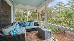 A covered outdoor seating area with a wicker sofa, patterned cushions, and a small table.